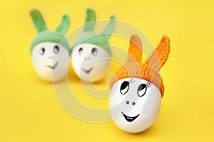 funny egg in orange cap with ears on yellow background and two eggs in green caps
