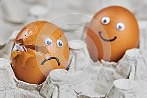 Funny egg and sad cracked egg in paper egg tray