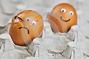 Funny egg and sad cracked egg in paper egg tray