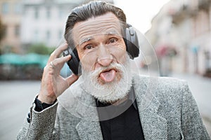 Funny elder man wearing headphones and showing tongue
