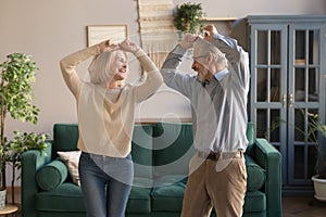 Funny elderly wife and husband raise hands dancing feels carefree