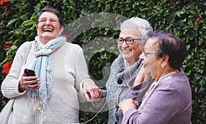 Funny elderly women listening to music on smartphone wearing earphones smiling enjoying fun celebrating retirement