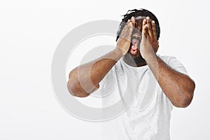 Funny emotive dark-skinned guy in white t-shirt fooling around and making faces while squeezing face, holding palms on