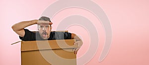 Funny emotive man sitting inside carton box and looking for big sales isolated on pink background. Black Friday