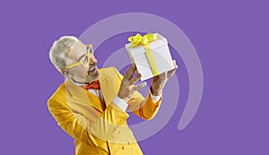 Funny excited senior man in amazement enjoys his gift isolated on purple background.