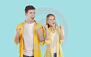 Funny excited young couple cheering and sincerely happy for their success on light blue background.
