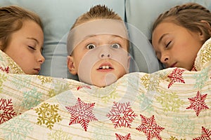 Funny expression on boys face between two cousins in bed