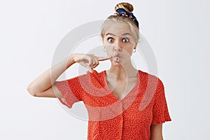 Funny expressive attractive blonde female student in vintage red polka-dot blouse and headband folding mouth in fish