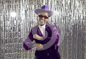 Funny extravagant young african american woman having fun dancing on shiny silver background.