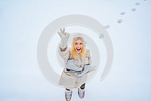 Funny face. Beautiful happy laughing young woman wearing winter hat gloves and scarf covered with snow flakes. Winter