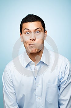 Funny face, goofy and portrait of comic man in studio isolated on blue background for expression. Comedy, humor and
