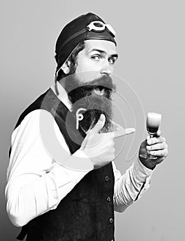 Funny face holding glass of alcoholic shot in vintage suede leather waistcoat with hat and glasses on blue studio