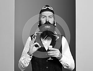 Funny face holding glass of alcoholic shot in vintage suede leather waistcoat with hat and glasses on colorful studio