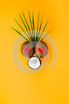 Funny face with in love, delighted expression with heart-shaped eyes made of coconuts and palm leaf on the orange background.