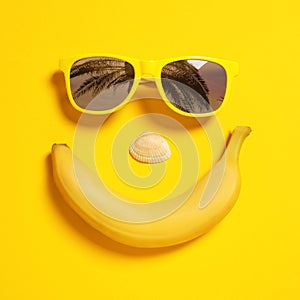 Funny face of sunglasses with reflection of palm trees, banana and seashell on yellow background