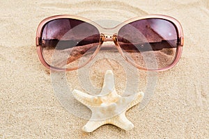 Funny face with sunglasses and sea star over sand background