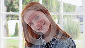 Funny face of teen redhead girl with freckles against white window