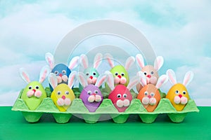 Funny faces easter bunny eggs in an egg carton green table blue sky