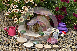 Funny fairy dollhouse on wooden planks by flowerbed with petunia flowers in the garden