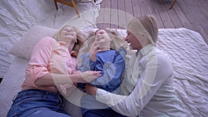 Funny family, happy mother with adult and little daughter fall on bed during fun laugh and tickle little girl