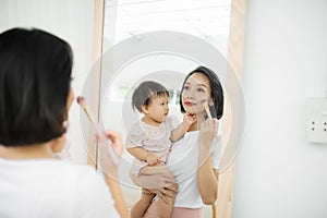 Funny family at home. Mother and her child girl are doing your makeup and having fun near mirror. Baby girl explores mother`s