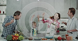 Funny family spending a good morning together in a modern kitchen dacing and playing with a pan , hand mixer, two boys