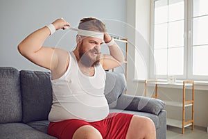 Funny fat angry man in sportswear is sitting on the sofa in the room