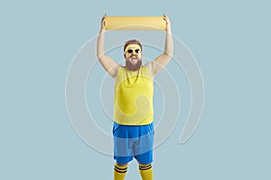 Funny fat man cheerfully lifts up sports mat rejoicing that he has finished doing sports training.