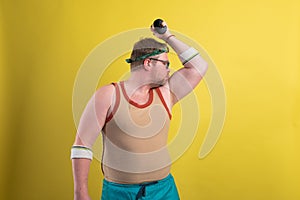 Funny fat man doing exercises with dumbbells. Overweight. yellow background