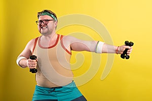 Funny fat man doing exercises with dumbbells. Overweight. yellow background