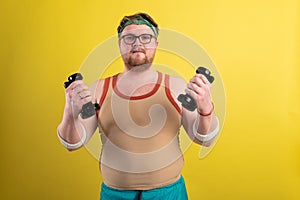 Funny fat man doing exercises with dumbbells. Overweight. yellow background