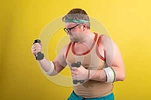 funny fat man doing exercises with dumbbells. Overweight. yellow background