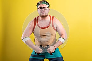 funny fat man doing exercises with dumbbells. Overweight. yellow background