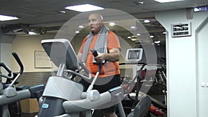 Funny fat man doing exercises on the ellipsoid in gym