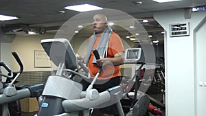 Funny fat man doing exercises on the ellipsoid in gym