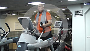 Funny fat man doing exercises on the ellipsoid in gym with hamburger