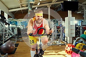 A funny fat man doing exercises on an exercise bike in a sports