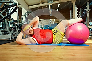 Funny fat man doing exercises on the floor in the gym.