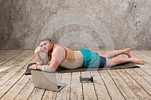 funny fat man doing sports on the yoga mat, doing sports online, looking into the laptop