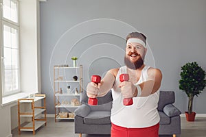 Funny fat man with dumbbells doing exercises in the room.