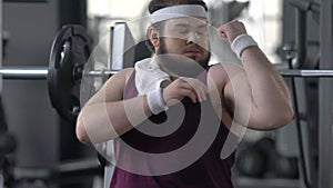 Funny fat man in gym pretending to have strong muscles, attracting attention