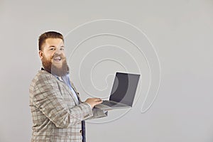 Funny fat man in a jacket works using a laptop while standing on a gray background.