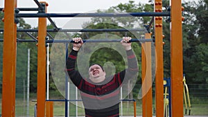 A funny fat man makes an effort to pull himself up on a horizontal bar.