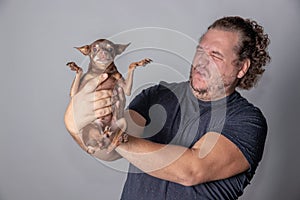 Funny fat man poses with little dog on gray background