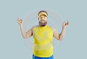 Funny fat man with serious facial expression meditating isolated on light blue background.