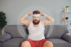 Funny fat man in sportswear is sitting on the sofa in the room