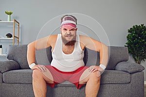 Funny fat man in sportswear is sitting on the sofa in the room