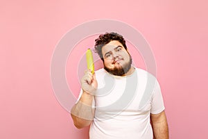 Funny fat man stands on a pink background with a banana in his hand, looks in camera and makes a funny face, wearing a white T-