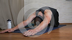 Funny fat man is trying to do yoga exercises on a mat on the background. Brutal male yogi