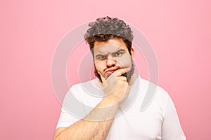 Funny fat man in white t-shirt looks into camera with pensive serious face on pink background, isolated. Funny pensive guy with